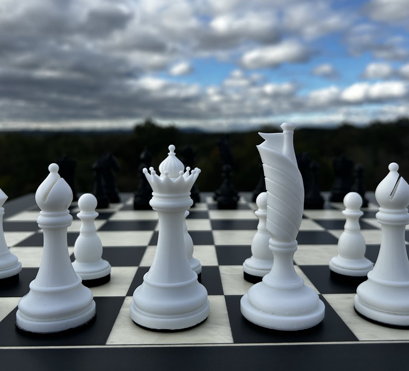 Close-up of the white Flag between the white queen and bishop, against clouds over a forested ridgeline